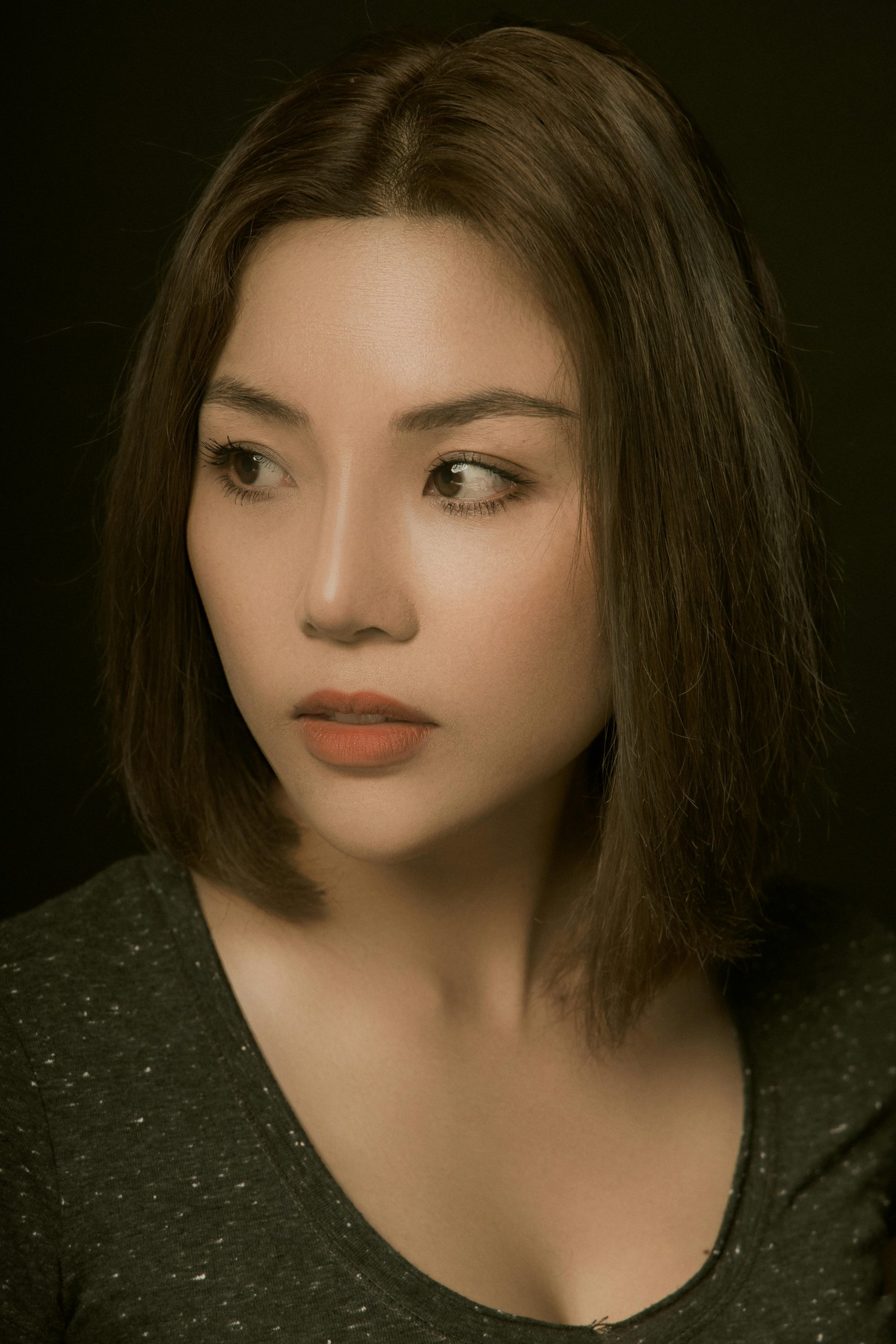 Portrait of an Asian woman gazing thoughtfully away, showcasing elegant makeup and hairstyle.