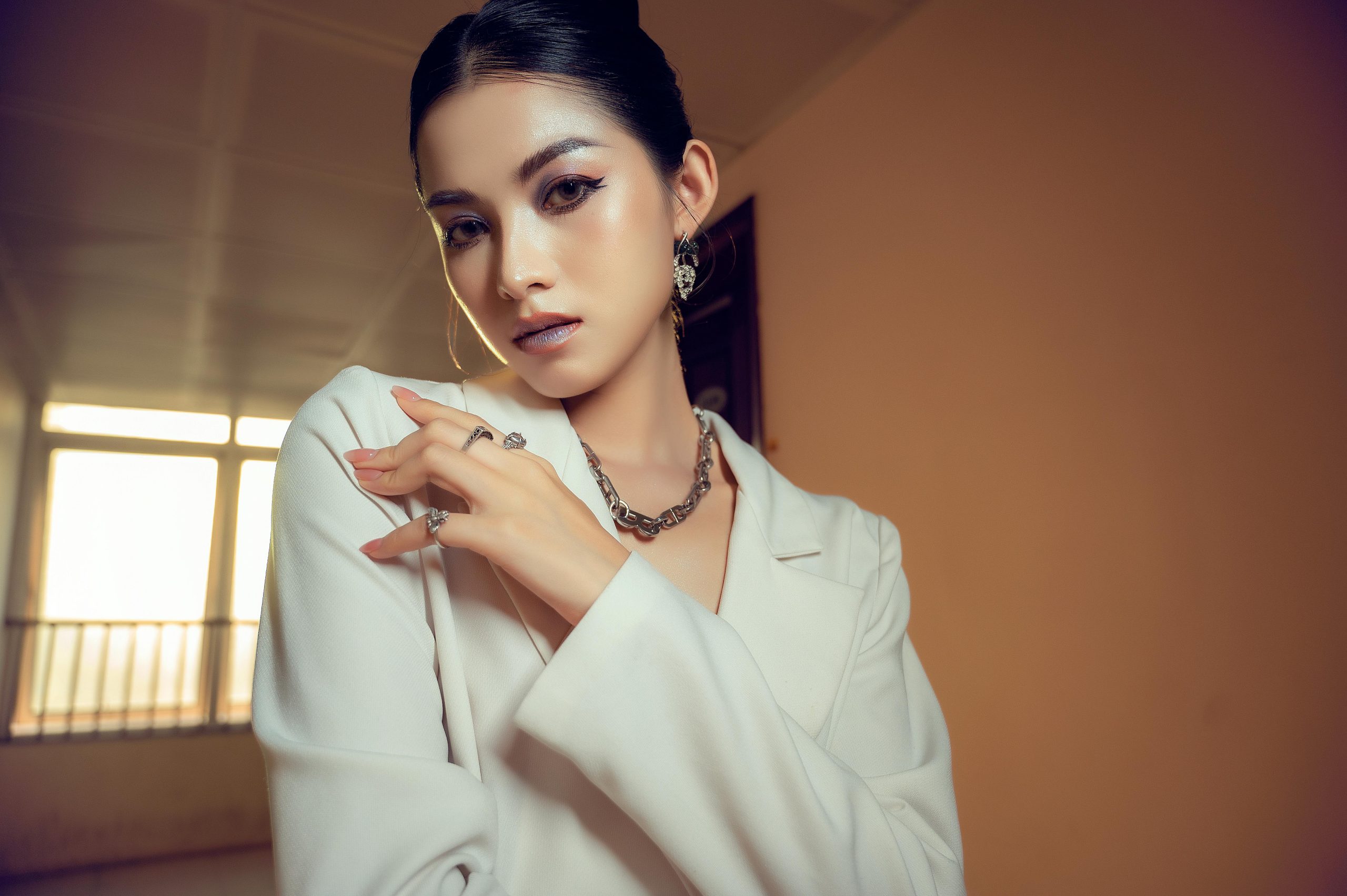 Stylish woman in white attire posing elegantly indoors with soft natural light.