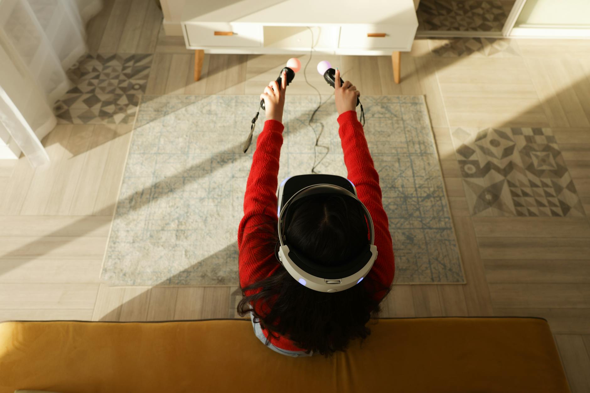 Overhead view of a woman wearing a VR headset and playing with controllers in a modern living room.
