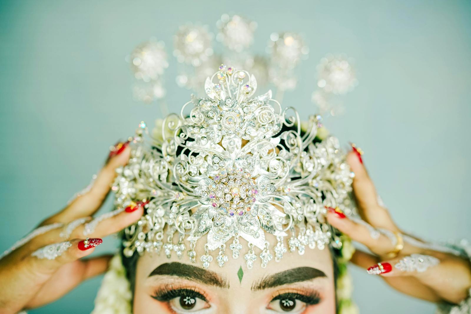 Close-up of a traditional silver bridal crown adorned with intricate details, showcasing elegant hand jewelry and manicure.